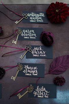 four key tags with names on them sitting next to some flowers and a red flower