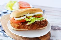 a fried chicken sandwich with lettuce tomato and onion on a wooden cutting board