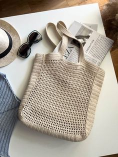 a bag, hat and sunglasses sitting on top of a white table next to an open book