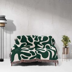 a green and white blanket sitting on top of a couch next to a floor lamp