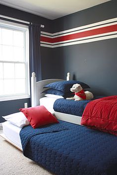 two beds in a room with blue walls and red pillows, one has a white dog sitting on the bed