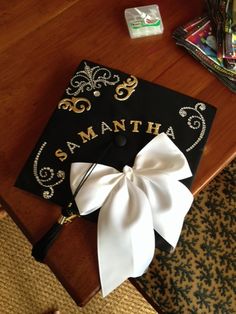 a black and gold graduation cap with a white bow on it sitting on a table