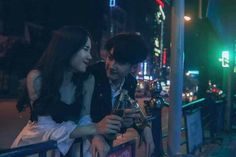 a man and woman standing next to each other on a city street at night with neon lights in the background