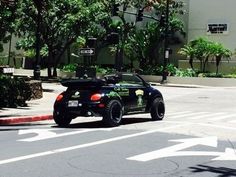 a black convertible car driving down a street next to a tall building with palm trees in the background