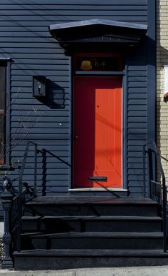 a red door is on the side of a gray building with black steps and railings