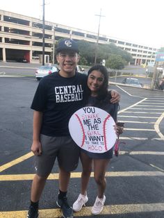 a man and woman standing in a parking lot holding a sign that says central baseball