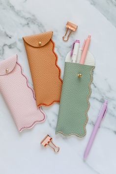 three leather pouches with pens and pencils on a marble counter top next to a pair of scissors