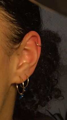 a close up of a person's ear with gold hoop earrings on it and hair in the background