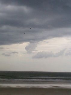 two people walking on the beach under an overcast sky