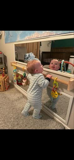 a baby standing in front of a mirror looking at himself in it's reflection