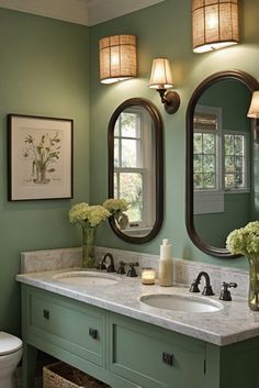 a bathroom with green walls and two round mirrors above the sink, along with flowers in vases on the counter