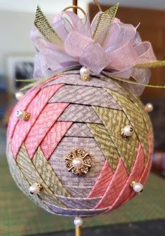 an ornament is decorated with pink, gold and white ribbons on a stand