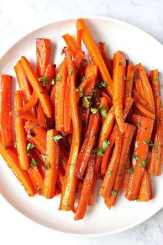 a white plate topped with sliced carrots on top of a marble countertop and garnished with parsley