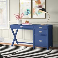 a blue desk with two drawers and a lamp on it in front of a white wall