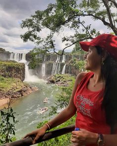 a woman wearing a red hat standing in front of a waterfall and looking at the water