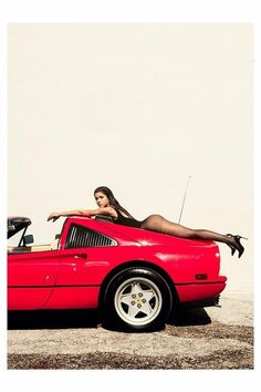 a woman in a red sports car with her foot on the hood and legs out