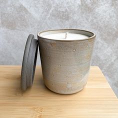 a white candle sitting on top of a wooden table next to a gray container with a lid