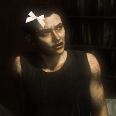 a man with a bow tie on his head sitting in front of a bookshelf