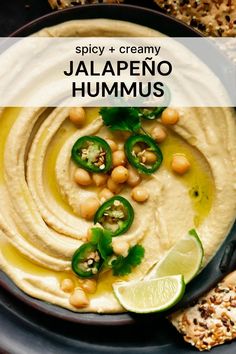 hummus in a black bowl with green peppers and sliced limes on the side