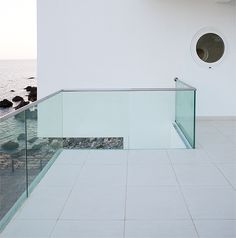 there is a glass railing on the side of a building by the water and rocks