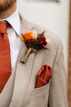 a man in a gray suit with an orange tie and boutonniere