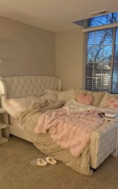 a white couch sitting in front of a window next to a book shelf on top of a bed