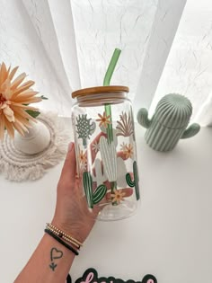 a person holding a glass jar with cactus designs on it