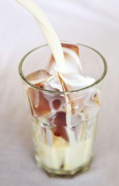 a glass filled with ice and milk being poured into it