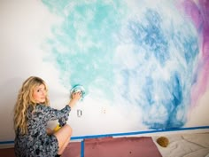 a woman is painting a wall with blue and pink paint