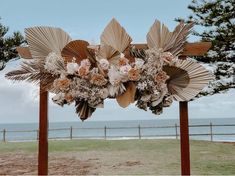 an outdoor ceremony setup with flowers and palm leaves on the altar by the ocean in front of a wooden fence