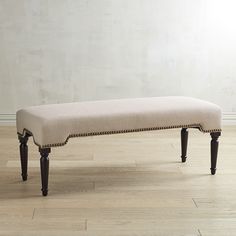 an upholstered bench in a room with white walls and wood flooring, along with hardwood floors