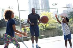 two children and an adult playing basketball on a court with buildings in the back ground