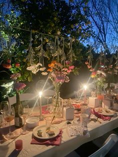 a table set for dinner with candles and flowers in vases on the table, surrounded by greenery