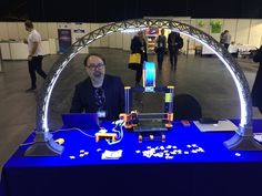 a man sitting in front of a laptop computer on top of a blue table covered in legos