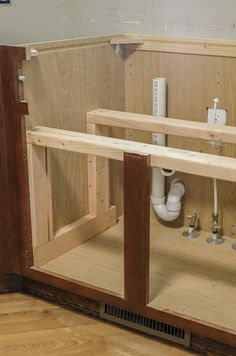 an unfinished kitchen cabinet with plumbing in the wall and wood flooring on the side