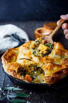 a hand holding a serving spoon over a quiche pie with cheese and spinach