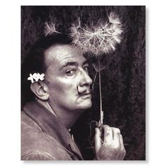 a black and white photo of a man holding a dandelion in front of his face