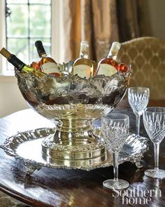 a glass bowl filled with bottles of wine on top of a table next to two glasses