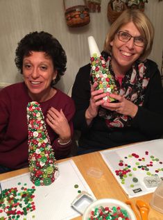 two women sitting at a table with christmas decorations on it and one holding up a bottle