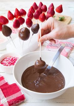 chocolate dipped strawberries are being dipped into melted chocolate in a white bowl on a wooden table