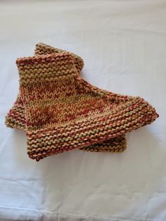 two knitted mittens sitting on top of a white bed sheet covered in blankets