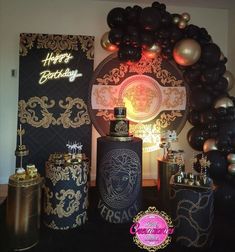 a table topped with lots of black and gold balloons next to bottles filled with liquor