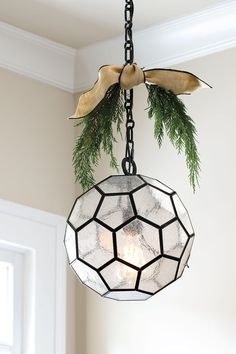 a light hanging from a ceiling with a bow on it's end and pine branches in the center