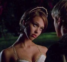 a woman in a white dress standing next to a man wearing a gold headband