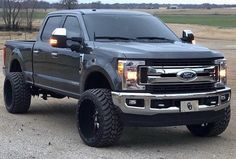 a large black truck parked on top of a gravel road next to a field and trees