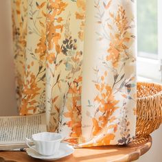 a cup and saucer sitting on a table next to a window with yellow curtains