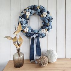 a wreath with blue and white balls hanging on the wall next to a vase filled with flowers