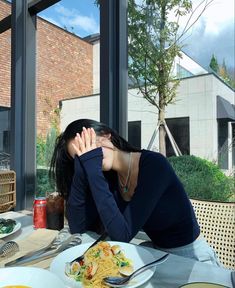 a woman sitting at a table in front of a plate of food with her hands on her face