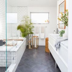 a white bathroom with black tile flooring and plants in the bathtub, along with two sinks