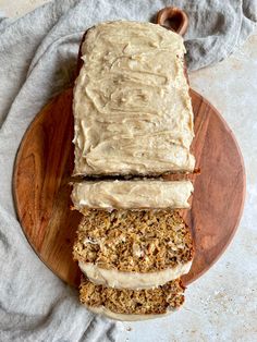 two slices of carrot bread with frosting on a wooden plate next to a gray towel